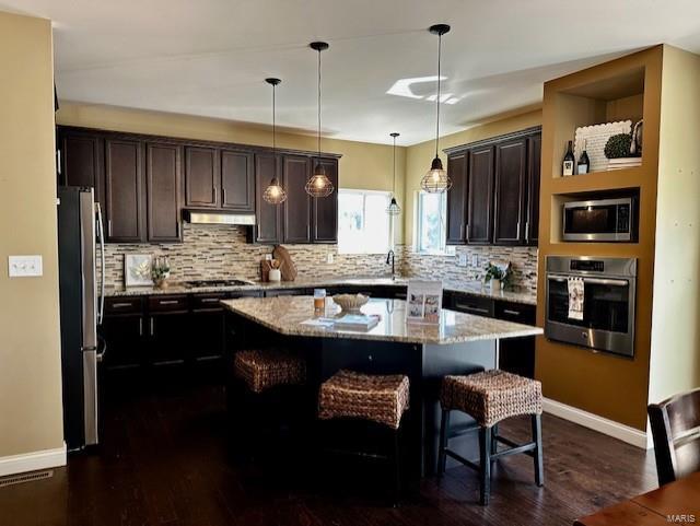 kitchen featuring a center island, dark brown cabinetry, under cabinet range hood, a breakfast bar, and stainless steel appliances