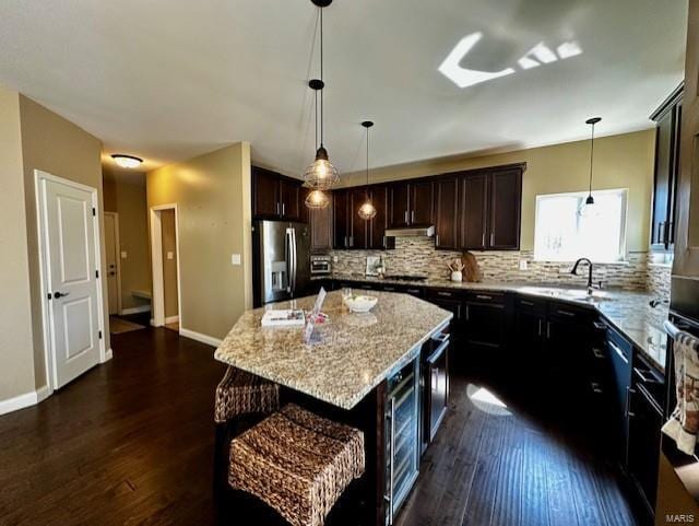 kitchen with light stone counters, a sink, dark wood-type flooring, under cabinet range hood, and stainless steel fridge