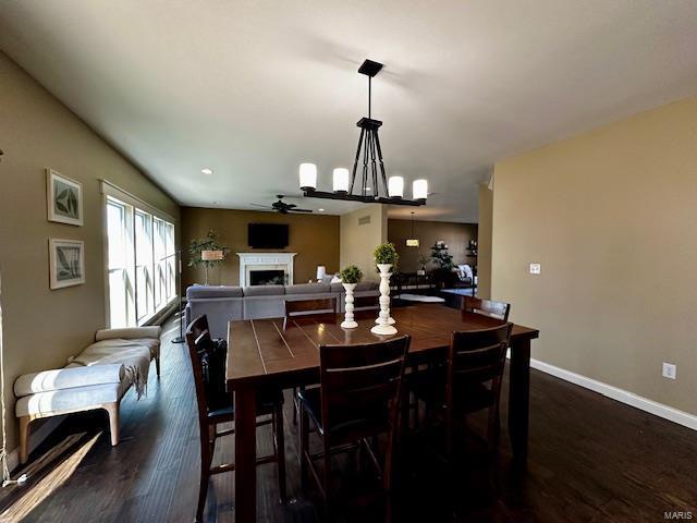 dining area featuring dark wood finished floors, a fireplace, baseboards, and a ceiling fan