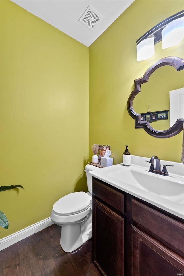 half bath with visible vents, toilet, wood finished floors, baseboards, and vanity