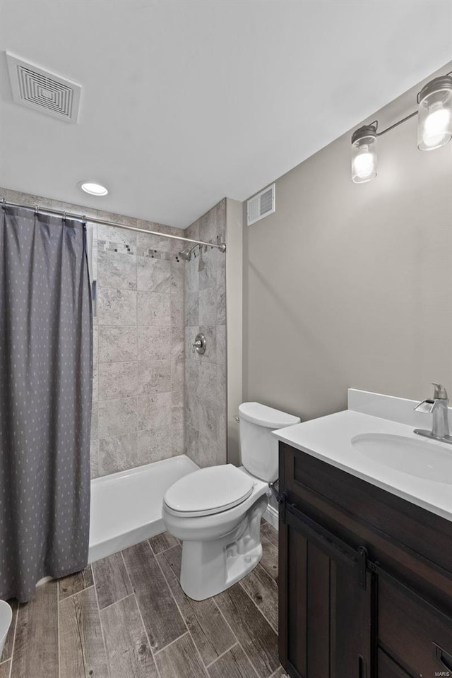 bathroom featuring a tile shower, visible vents, toilet, and wood finish floors