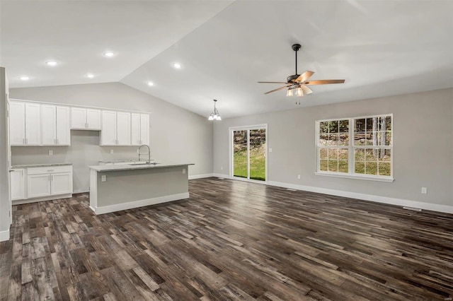 kitchen with lofted ceiling, dark hardwood / wood-style floors, ceiling fan with notable chandelier, white cabinetry, and a center island with sink