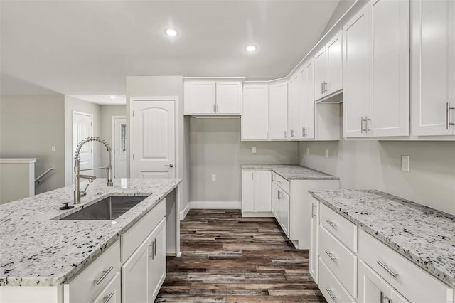 kitchen with light stone counters, dark wood-type flooring, sink, and white cabinets