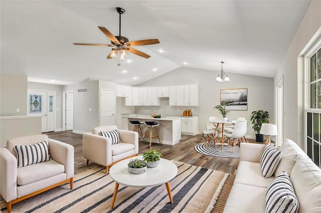 living room with ceiling fan with notable chandelier, lofted ceiling, and hardwood / wood-style flooring