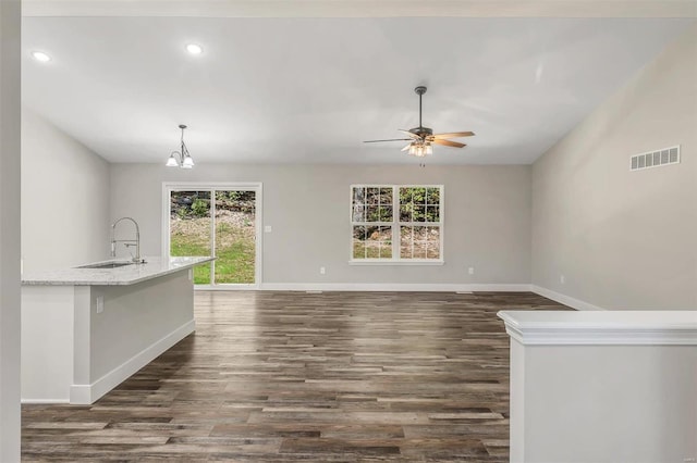 unfurnished living room featuring dark wood-type flooring, ceiling fan with notable chandelier, and sink