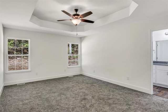 unfurnished room featuring ceiling fan, a tray ceiling, and dark carpet