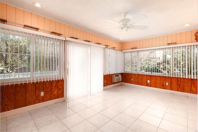 tiled spare room featuring ceiling fan, wooden walls, a healthy amount of sunlight, and an AC wall unit