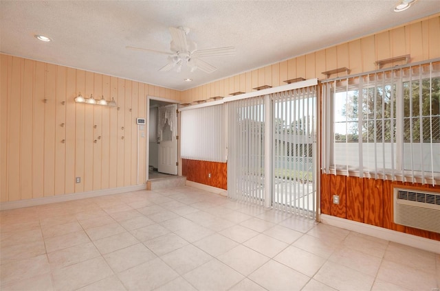 tiled empty room with ceiling fan, wood walls, a wall mounted AC, and a textured ceiling