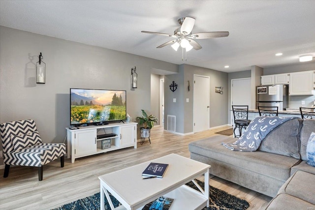 living room featuring light wood-type flooring, a textured ceiling, and ceiling fan