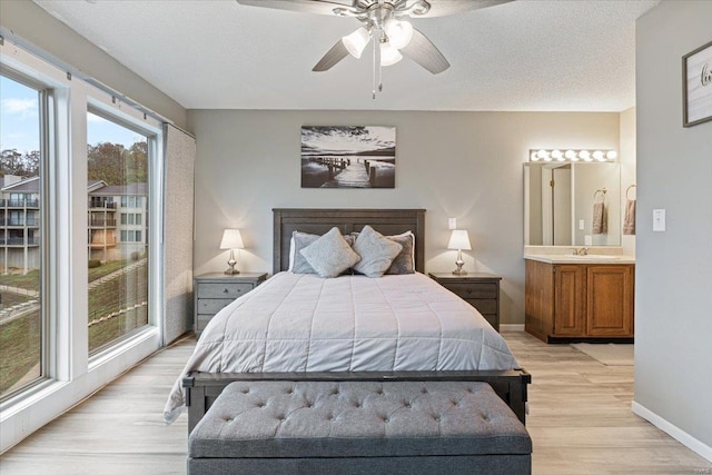 bedroom with light wood-type flooring, a textured ceiling, access to exterior, sink, and ceiling fan