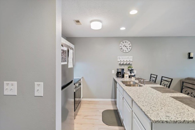 kitchen with white cabinetry, sink, appliances with stainless steel finishes, light stone countertops, and light wood-type flooring