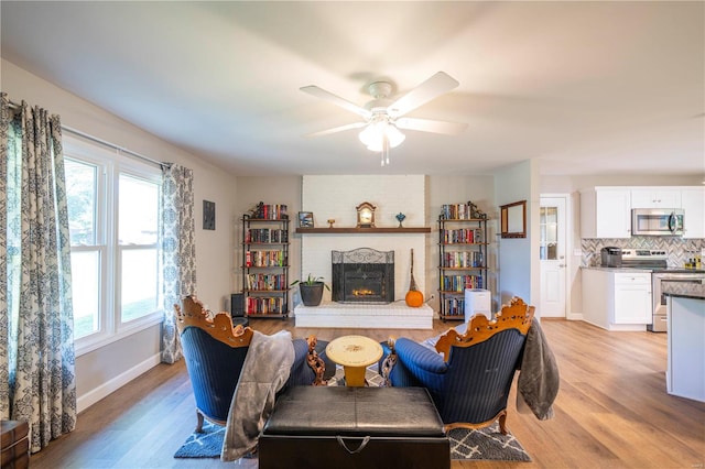 living room featuring ceiling fan, light wood-type flooring, and a fireplace