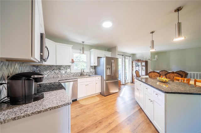 kitchen with dark stone countertops, white cabinetry, light hardwood / wood-style flooring, appliances with stainless steel finishes, and decorative light fixtures