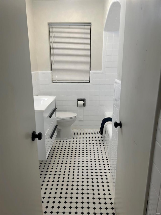 bathroom featuring tile patterned flooring, vanity, tile walls, and toilet