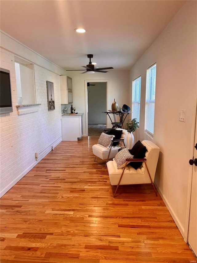 sitting room with ceiling fan, light wood-type flooring, and brick wall