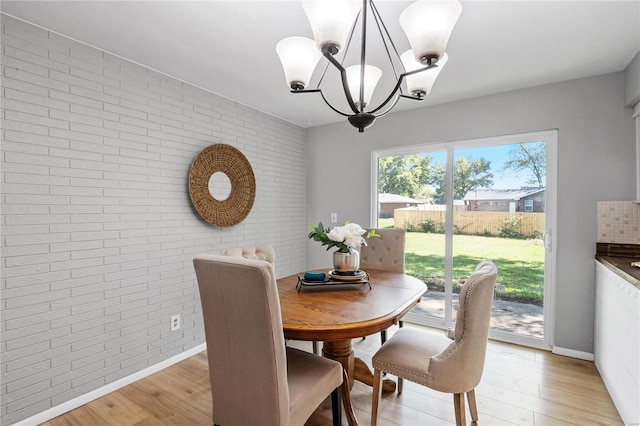 dining room with a chandelier, brick wall, and light hardwood / wood-style flooring