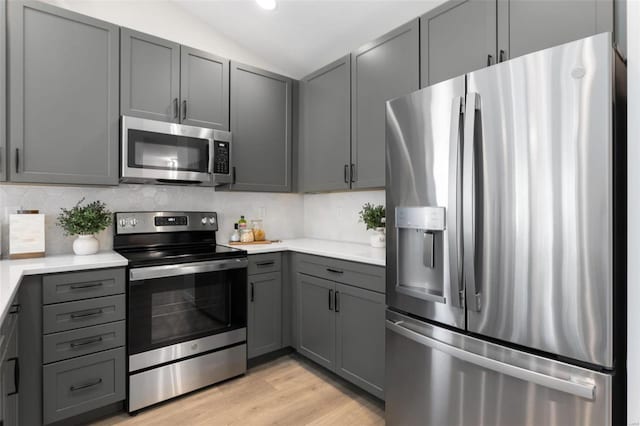 kitchen featuring gray cabinetry, tasteful backsplash, light hardwood / wood-style flooring, vaulted ceiling, and stainless steel appliances