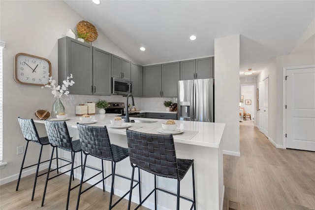 kitchen featuring lofted ceiling, kitchen peninsula, appliances with stainless steel finishes, a kitchen breakfast bar, and light hardwood / wood-style floors