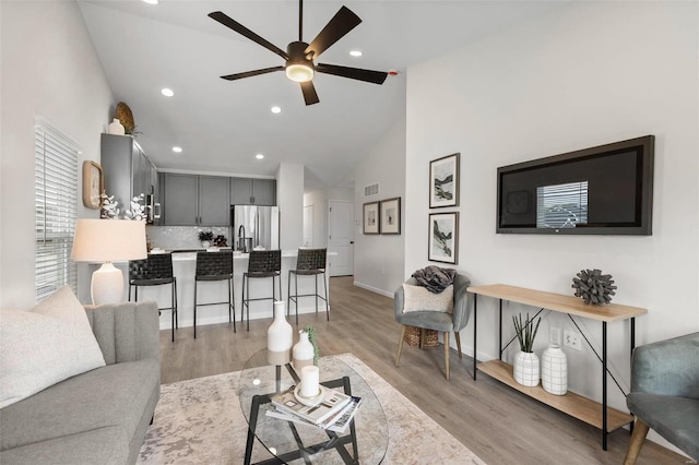 living room with ceiling fan, light wood-type flooring, and high vaulted ceiling