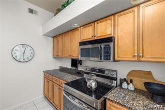 kitchen featuring stainless steel appliances, light tile patterned floors, and dark stone counters