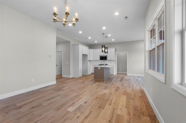 kitchen with stainless steel microwave, light wood-style flooring, open floor plan, a kitchen island with sink, and baseboards