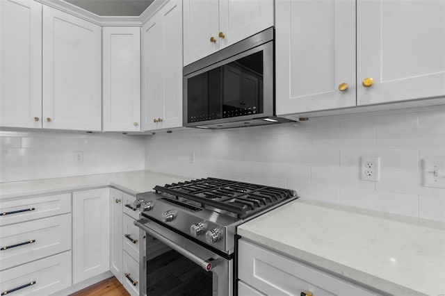 kitchen with light stone counters, stainless steel appliances, white cabinetry, light wood-style floors, and tasteful backsplash