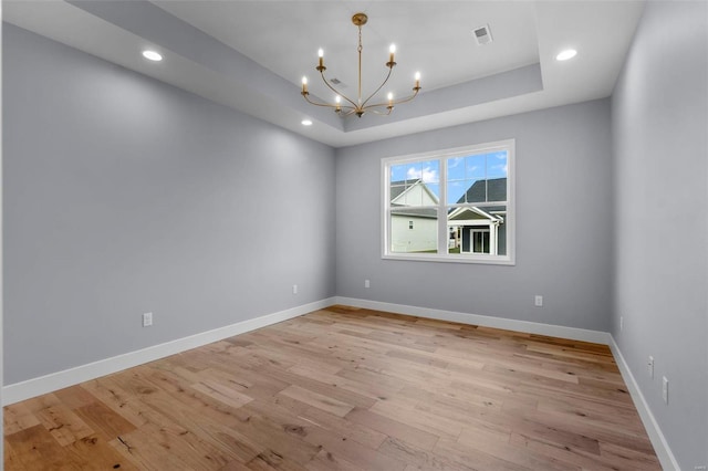 unfurnished room featuring a chandelier, a raised ceiling, light wood-style flooring, and baseboards