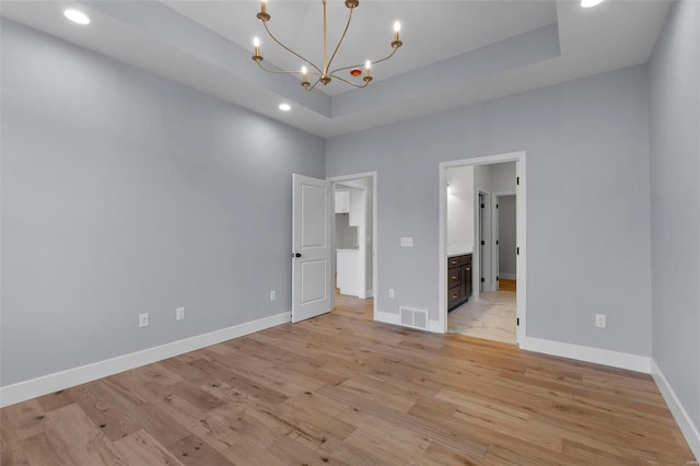 unfurnished bedroom featuring light wood-type flooring, a raised ceiling, visible vents, and baseboards