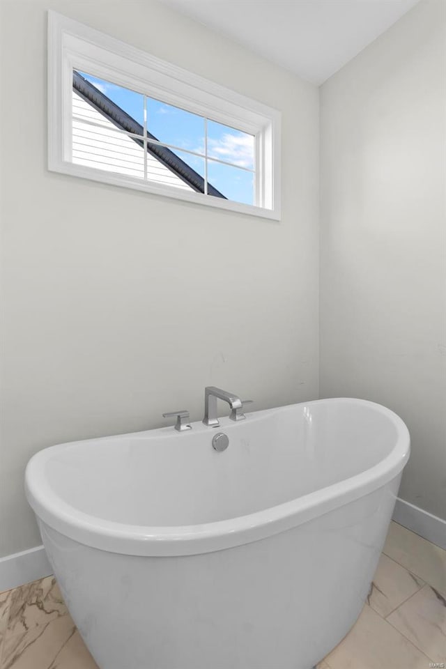 full bathroom featuring a healthy amount of sunlight, marble finish floor, baseboards, and a freestanding bath