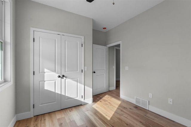 unfurnished bedroom with baseboards, visible vents, ceiling fan, wood finished floors, and a closet