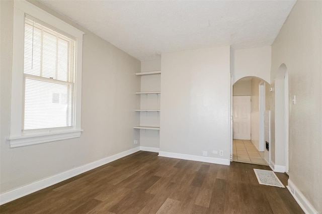 unfurnished room featuring a textured ceiling, a healthy amount of sunlight, and dark hardwood / wood-style flooring