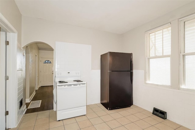 kitchen with white range with electric stovetop, tile walls, light tile patterned floors, and black fridge