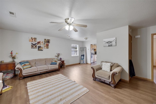 living room featuring ceiling fan, a textured ceiling, and light hardwood / wood-style floors