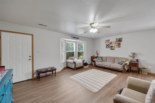 living room with ceiling fan, a textured ceiling, and light hardwood / wood-style floors