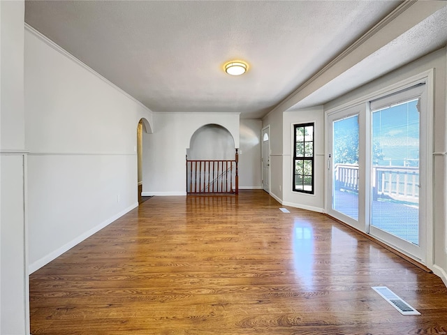 empty room with wood-type flooring, crown molding, and a textured ceiling