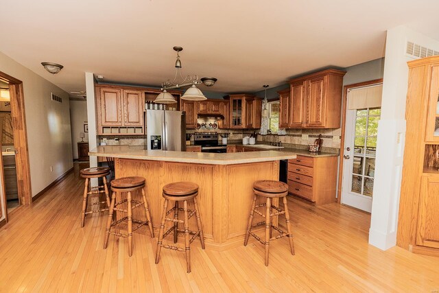 kitchen featuring tasteful backsplash, appliances with stainless steel finishes, decorative light fixtures, and light hardwood / wood-style flooring