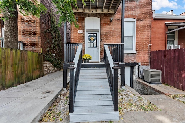 entrance to property with brick siding, fence, and central AC