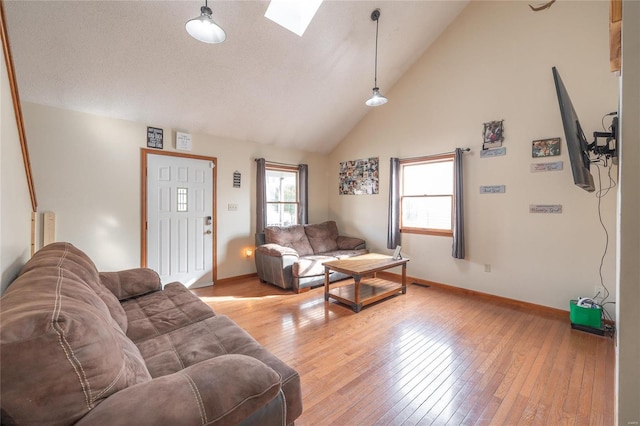 living room featuring a skylight, high vaulted ceiling, and light wood-type flooring