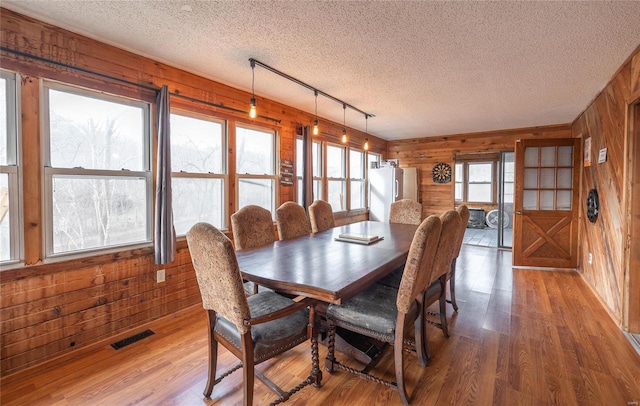 dining space featuring hardwood / wood-style floors, a textured ceiling, a healthy amount of sunlight, and wood walls