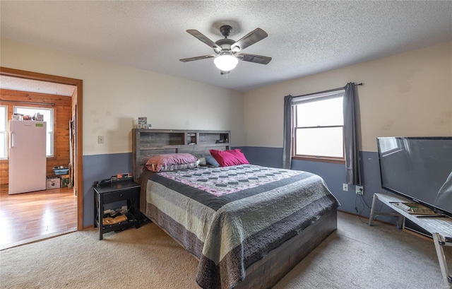 carpeted bedroom with multiple windows, a textured ceiling, white refrigerator, and ceiling fan