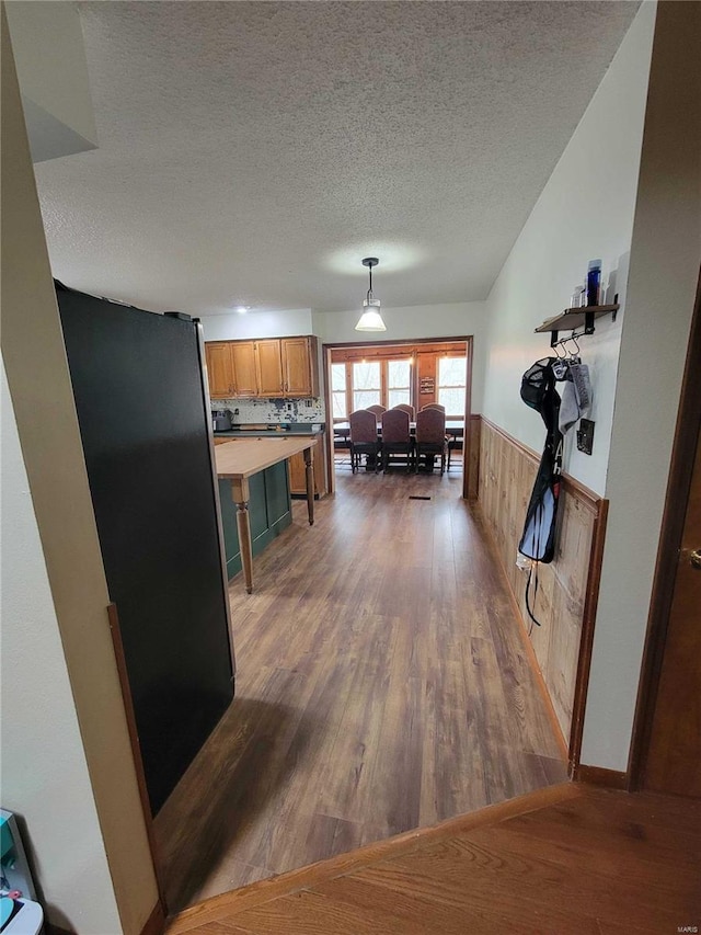 kitchen with a wainscoted wall, a textured ceiling, brown cabinets, and wood finished floors