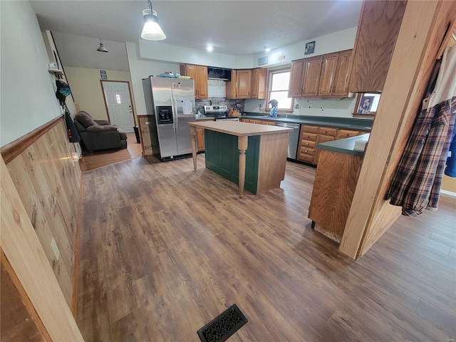 kitchen featuring stainless steel appliances, wainscoting, wood finished floors, and visible vents