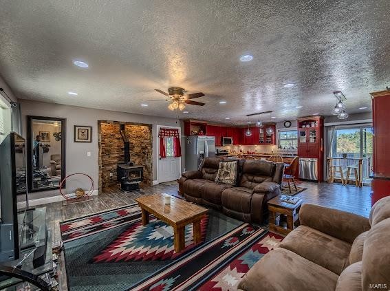 living room with ceiling fan, a textured ceiling, and a wood stove