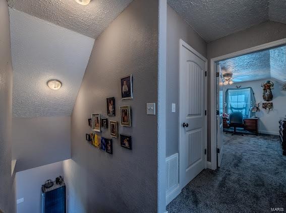 corridor featuring carpet floors, vaulted ceiling, and a textured ceiling