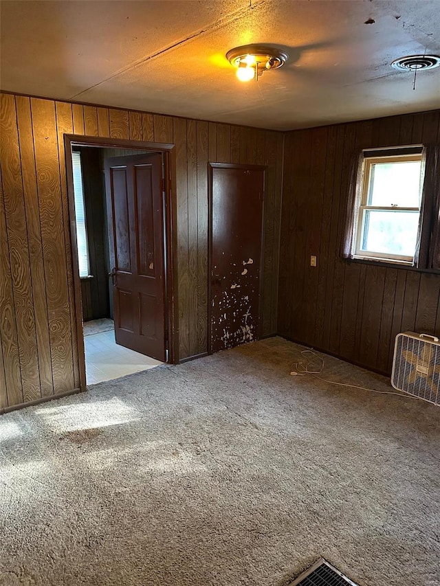 unfurnished bedroom with light colored carpet, a textured ceiling, and wood walls