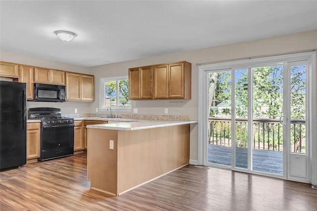 kitchen with light wood-type flooring, black appliances, kitchen peninsula, and sink