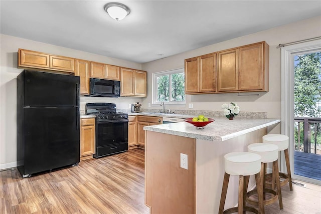 kitchen featuring light hardwood / wood-style floors, a kitchen bar, black appliances, and kitchen peninsula