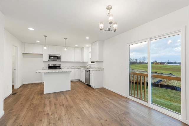 kitchen featuring light stone counters, white cabinets, pendant lighting, stainless steel appliances, and light hardwood / wood-style floors