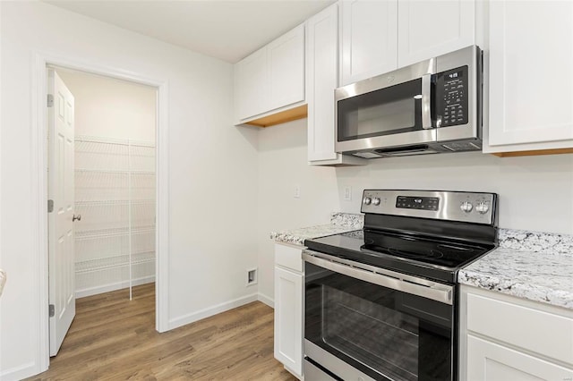 kitchen with light stone countertops, stainless steel appliances, light wood-type flooring, and white cabinetry