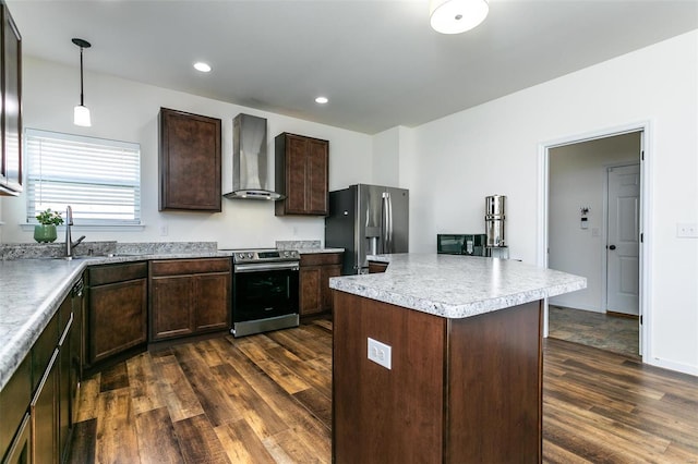 kitchen with wall chimney range hood, appliances with stainless steel finishes, dark wood-type flooring, pendant lighting, and a center island